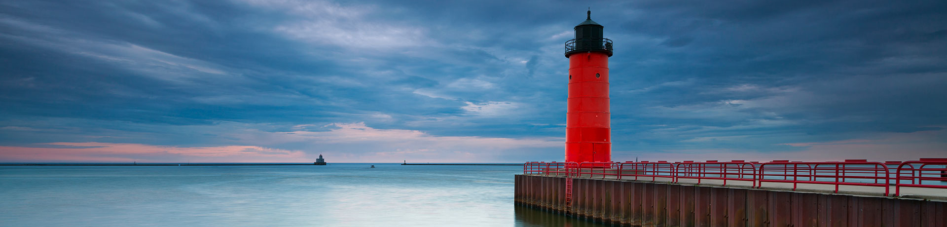Un grand phare rouge sur les côtes avec un ciel nuageux bleuté